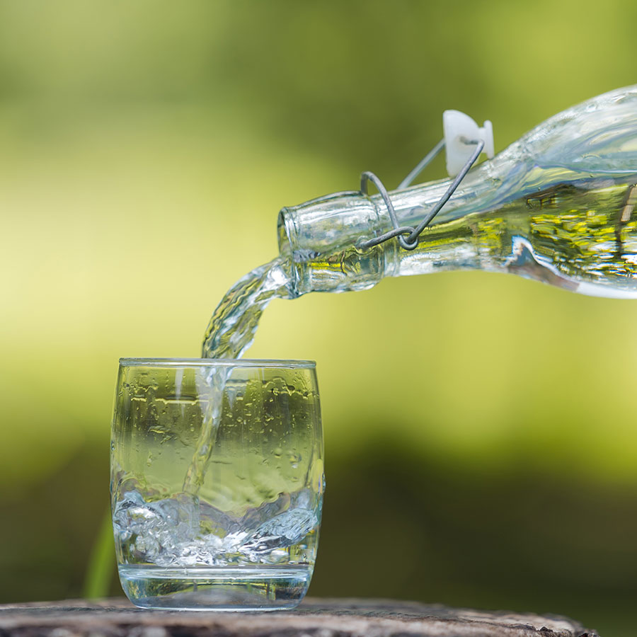 Aus einer Bügelverschlussflasche wird Wasser in ein Glas gegossen